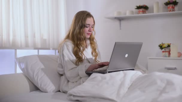早朝からノートパソコンで働くかわいい女の子、バスローブに身を包み、フリーランス — ストック動画