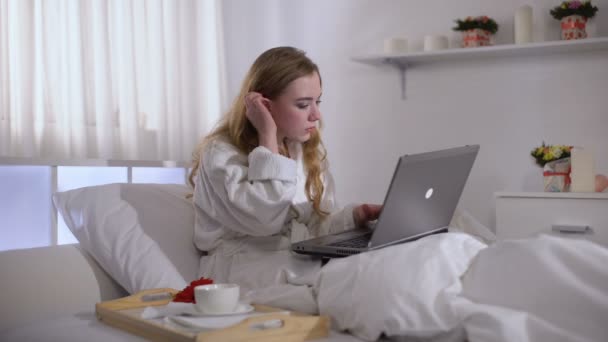 Flicka i Robe dricka kaffe i sängen och arbetar på laptop, frilans koncept — Stockvideo