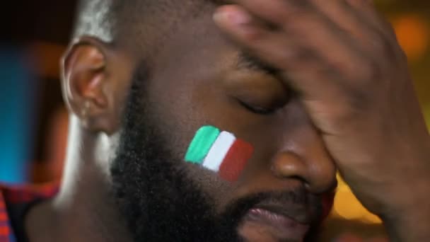 Schwarzer männlicher Fan mit italienischer Fahne auf der Wange ärgert sich über das verlorene Spiel seiner Lieblingsmannschaft — Stockvideo