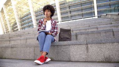 Ödev, arena yakınındaki merdivenlerde oturan sevimli kıvırcık saçlı kız öğrenci