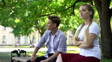 Offended teen couple sitting in park on bench, ignoring each other, conflict clipart