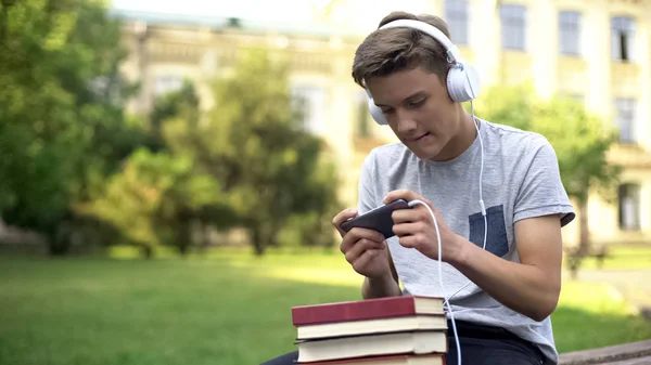 十代の少年のヘッドフォン 先延ばしの宿題代わりにモバイル ゲームをプレイ — ストック写真