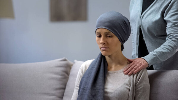 Mother putting hand on shoulder of her upset daughter with cancer, support