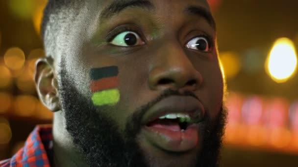 Afro-americano fã de futebol regozijando vitória da equipe favorita, bandeira alemã na bochecha — Vídeo de Stock