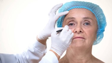 Anti-aging tedavisi öncesi yaşlı kadın yüzüne işaret ler çizen plastik cerrah