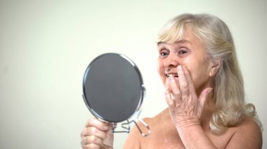 İyimser yaşlı kadın kadınsı aynaya bakmak Anti-Aging Krem uygulamak
