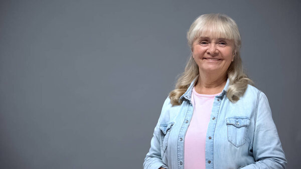 Positive elderly lady in casual clothes isolated on gray, happy secure old age