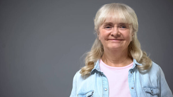 Smiling elderly lady in casual clothes isolated on gray, happy secure old age