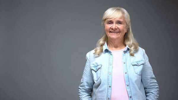 Old lady smiling into camera, looks healthy and trendy in casual denim clothes