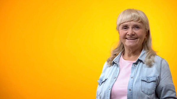 Smiling old lady posing against bright background, positive attitude to life