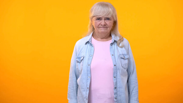 Elderly female with serious look isolated on orange template, retirement age
