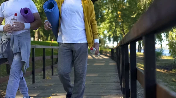 ヨガマットとウォーターボトル ワークアウトで公園を歩くスポーティな成熟した男性 — ストック写真