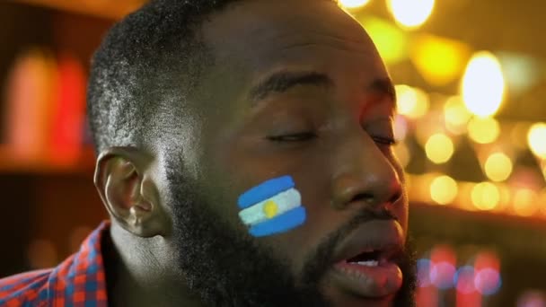 Schwarzer Sportfan mit argentinischer Fahne auf der Wange ärgert sich über Niederlage seiner Lieblingsmannschaft — Stockvideo