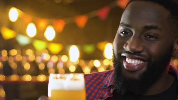 Alegre hombre afroamericano tintineo vaso de cerveza, fiesta de la noche celebración — Vídeo de stock