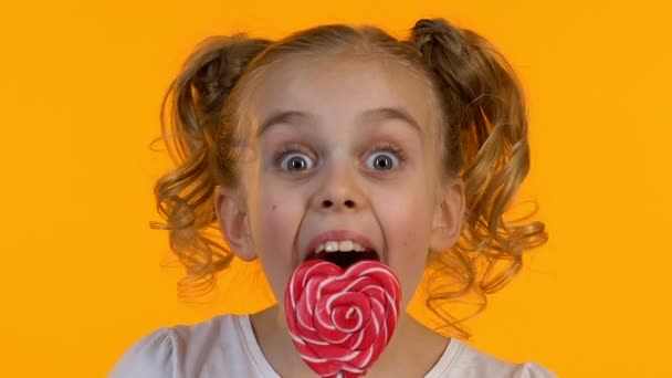 Rendkívül boldog kislány élvezi íze szív alakú nyalóka, közelről — Stock videók