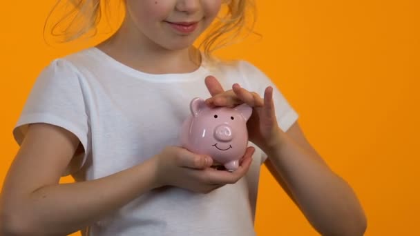 Menina acariciando porquinho banco, poupança pessoal e orçamento, planejamento futuro — Vídeo de Stock
