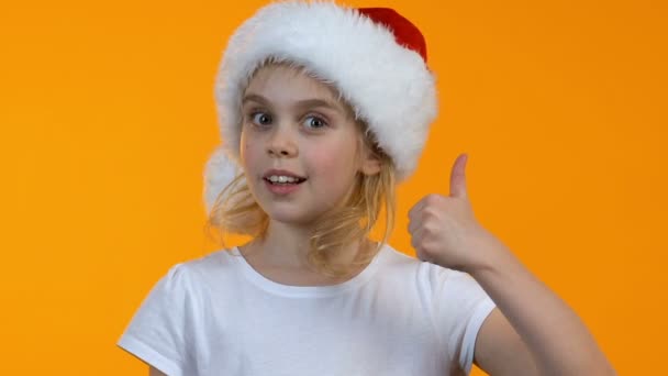 Kleine vrouwelijke Kid in Santa hoed weergegeven duimen-up en winking op camera, vakantie — Stockvideo