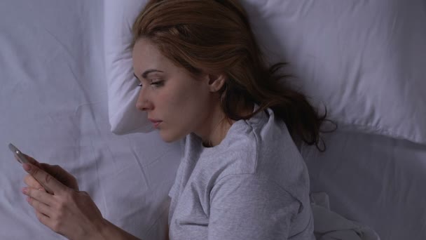 Χαρούμενη Κυρία συνομιλεί με smartphone με αγαπημένη, ξαπλωμένη στο κρεβάτι, τρυφερές σχέσεις — Αρχείο Βίντεο
