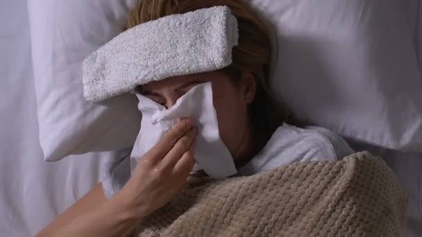 Mujer enferma con toalla en la frente acostada en la cama, tos y sonarse la nariz, gripe — Vídeo de stock