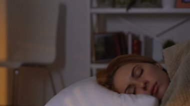 Kadın rahat bir yatakta uyuyor, sabah güneşi dışarıda, sağlıklı bir rüya.