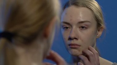 Genç ağlayan kız aynada yüzüne bakıyor, cilt problemleri çekiyor.