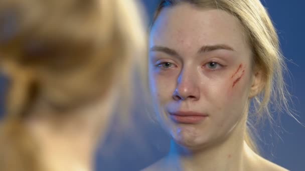 Teen girl with wounded face looking at mirror reflection and deeply crying — Stock Video