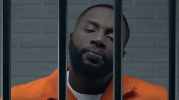 Confident Afro-American criminal in prison cell looking at camera with contempt — Stock Video