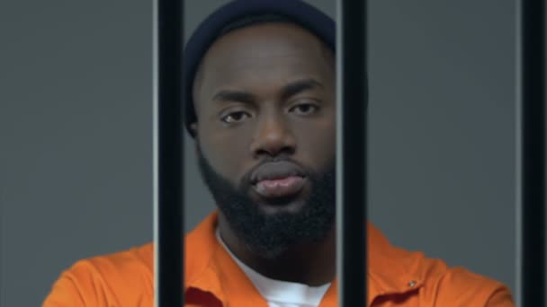 Επικίνδυνος Αφρο-Αμερικανός καταδικασμένος άνθρωπος που κοιτάζει την κάμερα μέσα από τα κάγκελα της φυλακής — Αρχείο Βίντεο