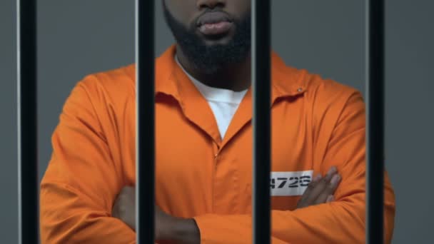 Svart brottsling med händerna korsade stående i fängelsecell, väntar på dom — Stockvideo