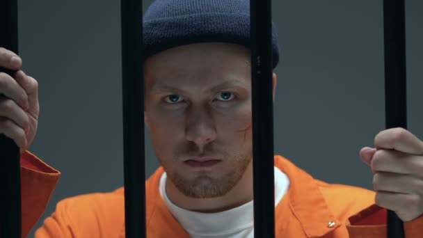 Σίγουρος κρατούμενος με ουλές στο πρόσωπο που δείχνει τα χέρια σε χειροπέδες στην κάμερα, το κελί — Αρχείο Βίντεο