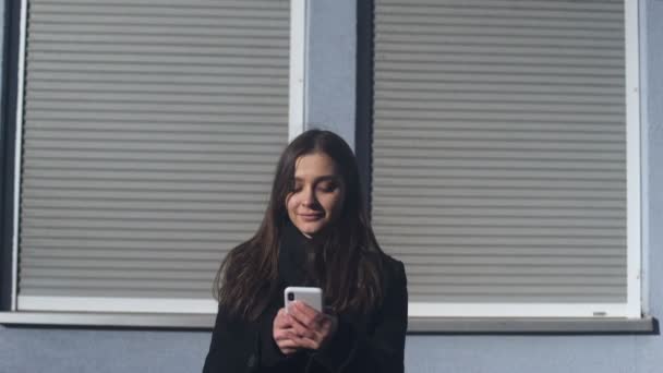 Hübsche junge Frau steht draußen und tippt auf dem Smartphone, macht Verabredung — Stockvideo