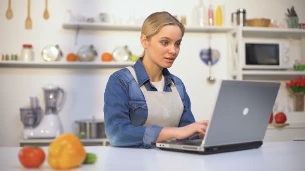 Menina bonita positivo procurando dicas de culinária na internet, novato na cozinha — Vídeo de Stock