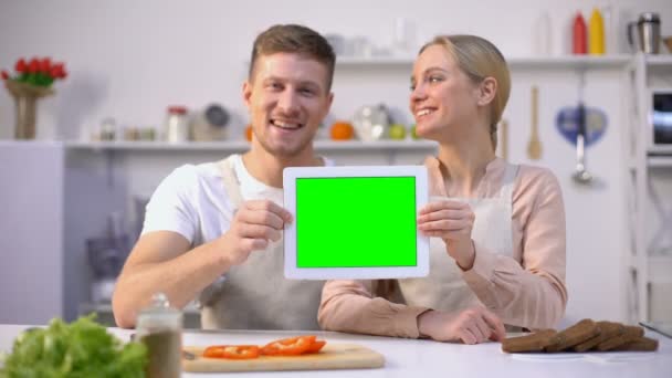 Молодая улыбающаяся пара показывает планшет с зеленым экраном, шаблон кулинарных курсов — стоковое видео