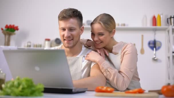 Casal jovem à procura de receitas de alimentos em sites e risos, novatos cozinha — Vídeo de Stock