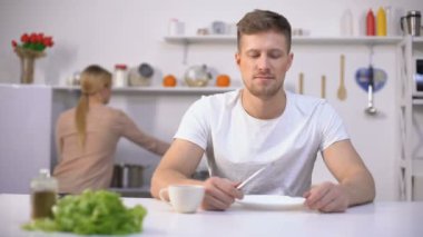 Olumlu adam akşam yemeği bekliyor, genç karısı arka planda çorba pişirme, açlık