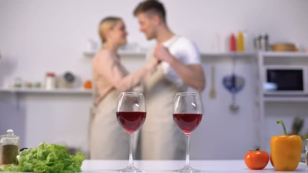 Бокалы для вина на столе, семейная пара танцует на заднем плане, кухонный интерьер — стоковое видео