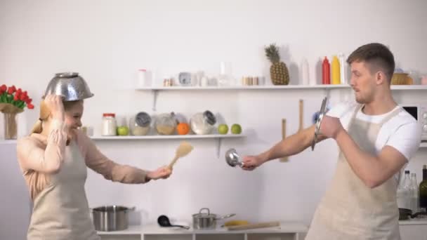 Беззаботная пара, дерущаяся с кухонной утварью, притворяющаяся рыцарем, развлекающаяся — стоковое видео