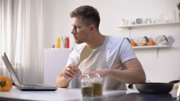 Junggeselle bereitet Mahlzeit in der Pfanne zu, liest online Rezepte und Kochtipps, Kurse — Stockvideo