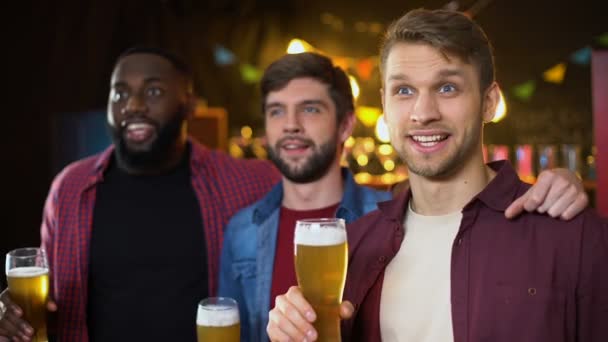 Alegre multiétnicos aficionados al fútbol tintineo vasos de cerveza, viendo el fútbol en el pub — Vídeo de stock
