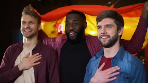 Aficionados al fútbol masculino multiétnico español cantando himno nacional y ondeando bandera — Vídeos de Stock