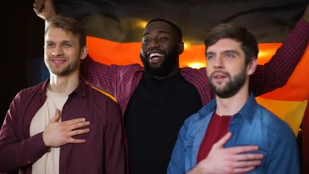 Multietniska tyska fotbollsfans sjunger hymn, vinka flagga i bar, supportrar — Stockvideo