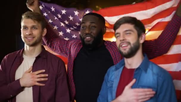 Патріотичні американські фани аплодують команді, співаючи гімн і розмахуючи прапором в пабі — стокове відео