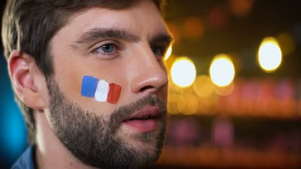 Feliz guapo barbudo francés ventilador con bandera pintada en la mejilla celebrando gol — Vídeo de stock