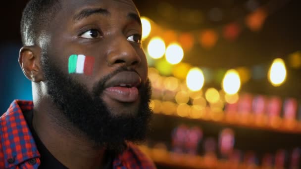 Чрезвычайно эмоциональный черный футбольный фанат с итальянским флагом на щеке кричать, гол — стоковое видео