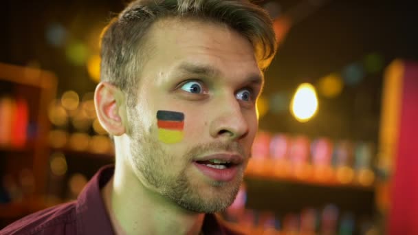 Веселый немецкий футбольный болельщик с флагом на щеке счастлив за команду забив гол, победа — стоковое видео