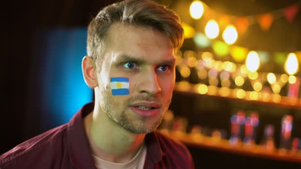 Футбольный болельщик с аргентинским флагом на щеке делает лицо, недовольный потерей — стоковое видео