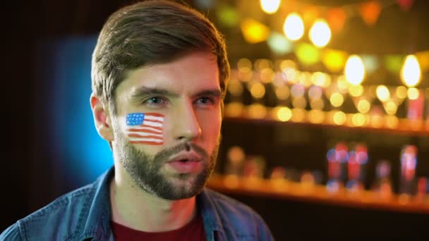 Extremadamente feliz fanático del fútbol americano con bandera en la mejilla haciendo sí gesto, ganar — Vídeo de stock