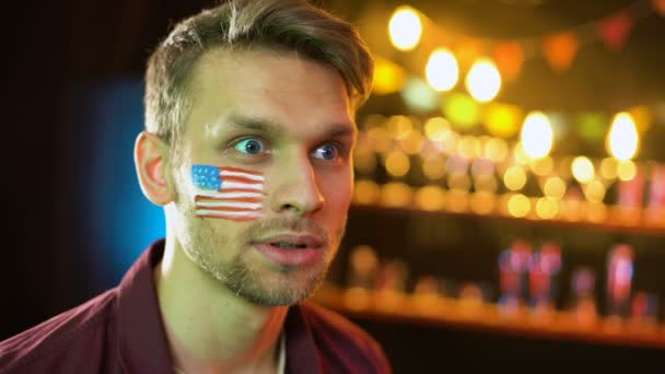 Эмоциональный американский футбольный фанат с флагом на щеке делает да жест, выиграть — стоковое видео