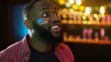 Yanağında bayrak lı Afro-Amerikan futbol taraftarı maçı kazanan takım için tezahürat yapıyor