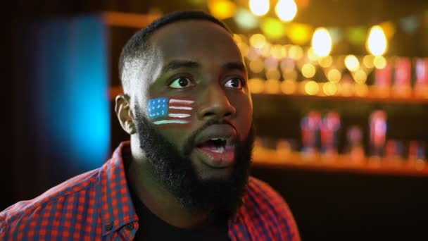 Нервный афро-американский футбольный фанат с флагом на щеке, недовольный результатом игры — стоковое видео